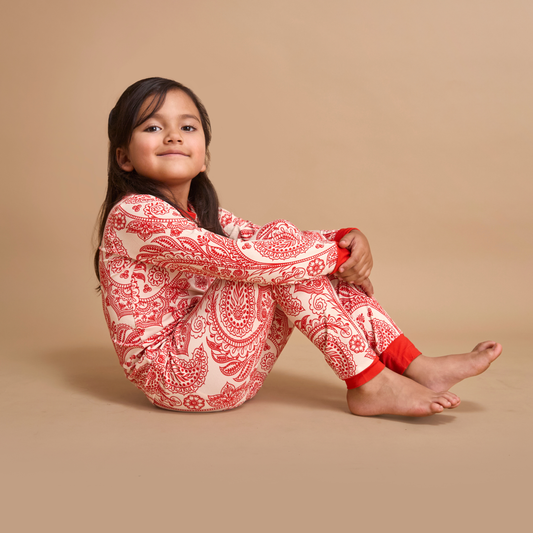 Young girl wearing red and white patterned pajamas sitting on a beige background