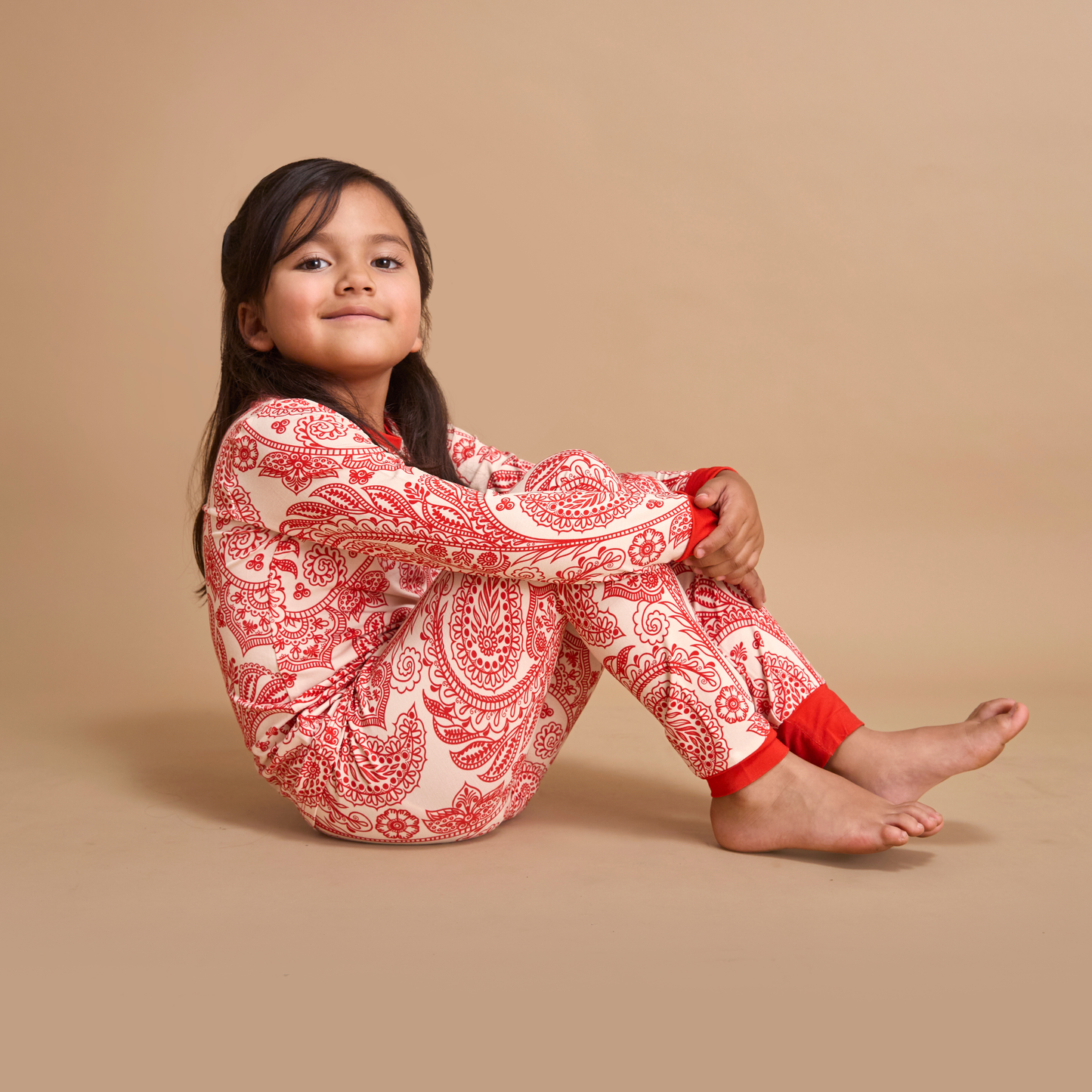 Young girl wearing red and white patterned pajamas sitting on a beige background