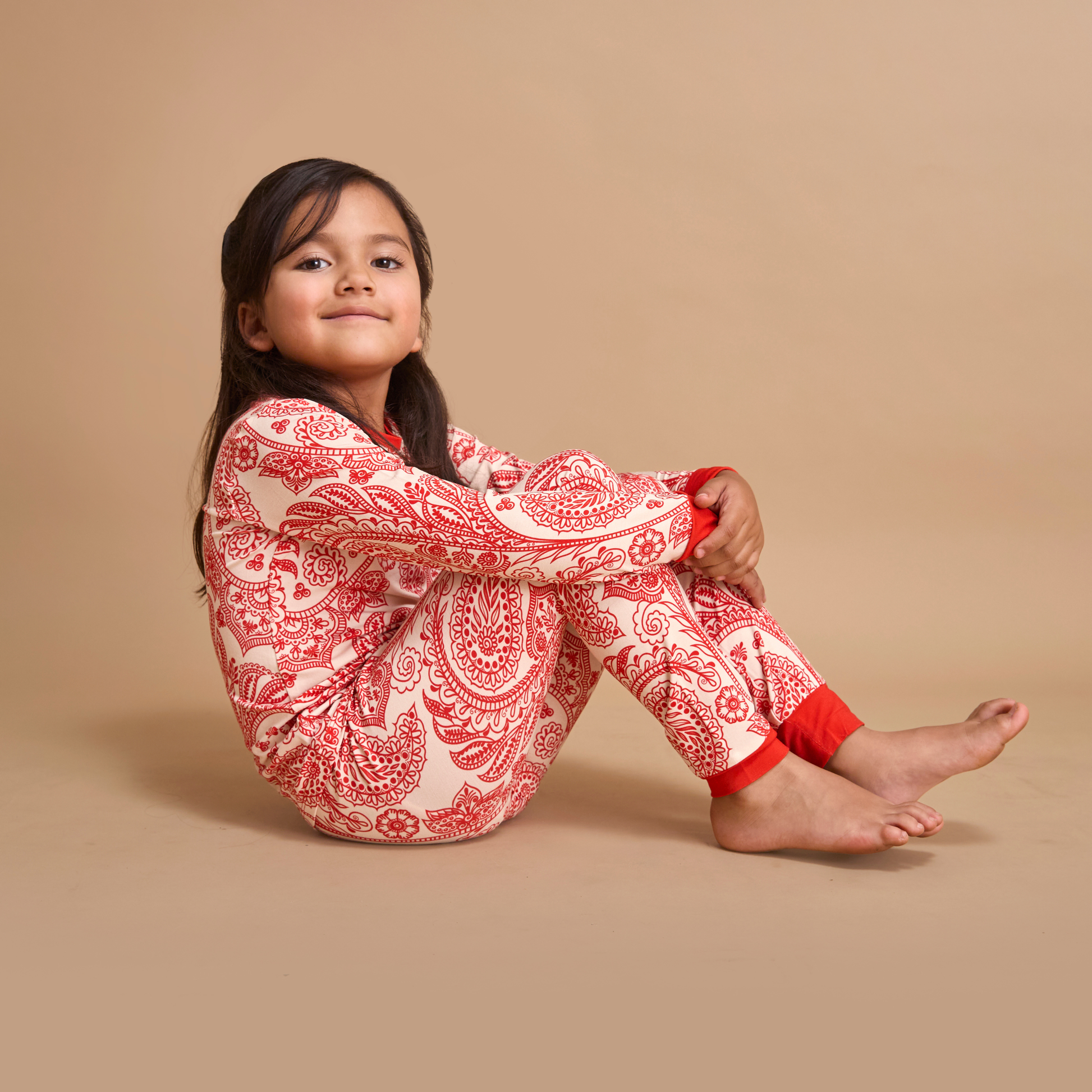Young girl wearing red and white patterned pajamas sitting on a beige background