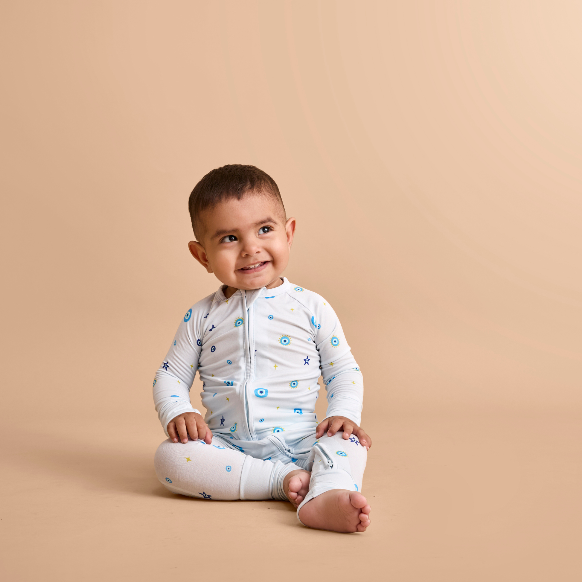 Baby wearing a white onesie with blue patterns on a beige background