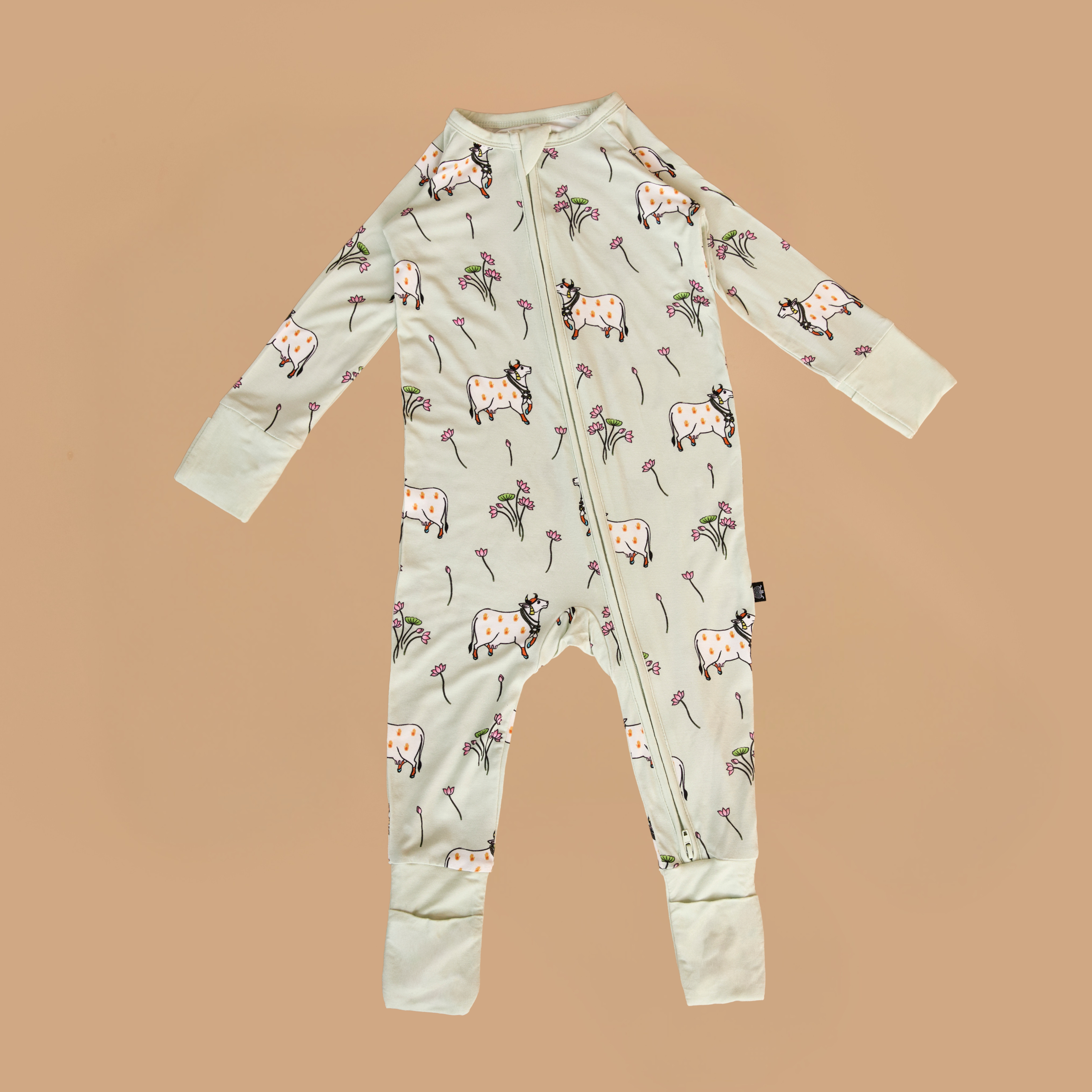 Pichwai Pastures baby zippered sleeper with hand-illustrated cow and lotus print on a beige background